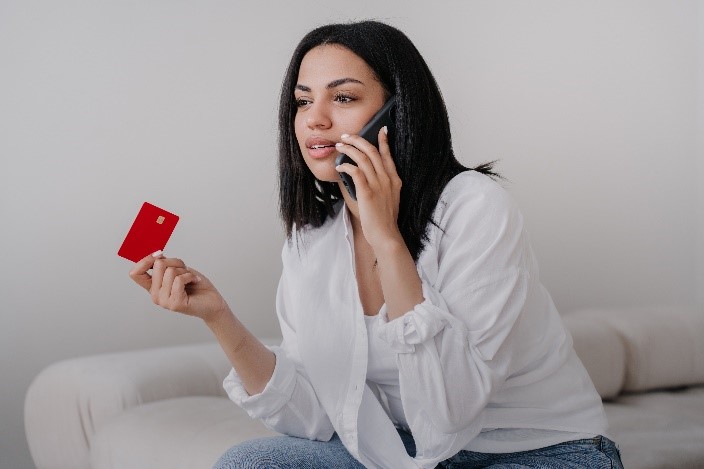 woman holding credit card talks on phone with financial institution